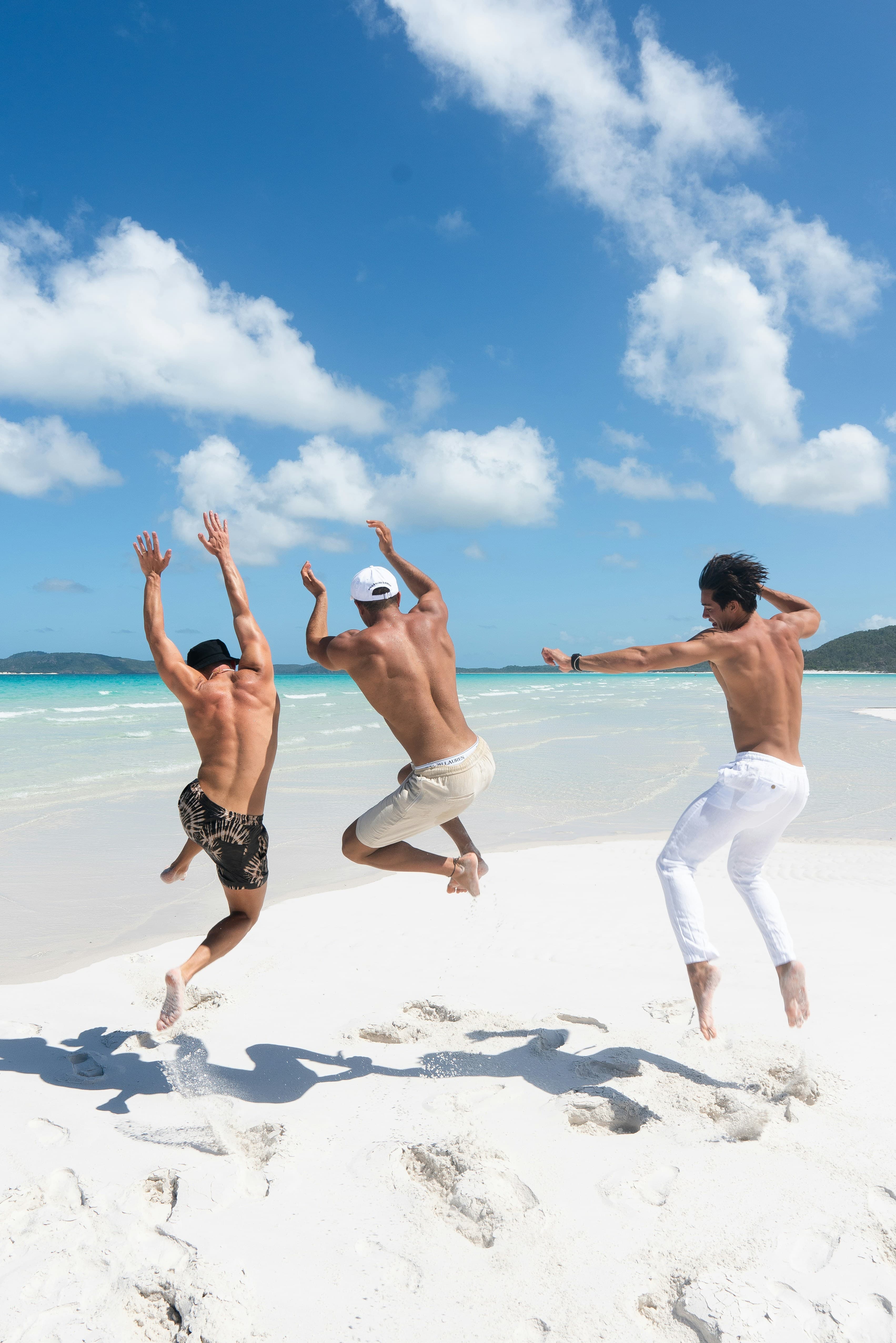 Trois voyageurs sautent de joie sur une plage de sable blanc